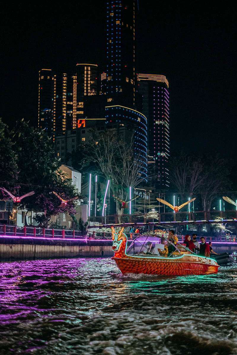 Perahu wisata berlampu melintas di Sungai Kalimas dengan latar gedung Kota Surabaya pada malam hari