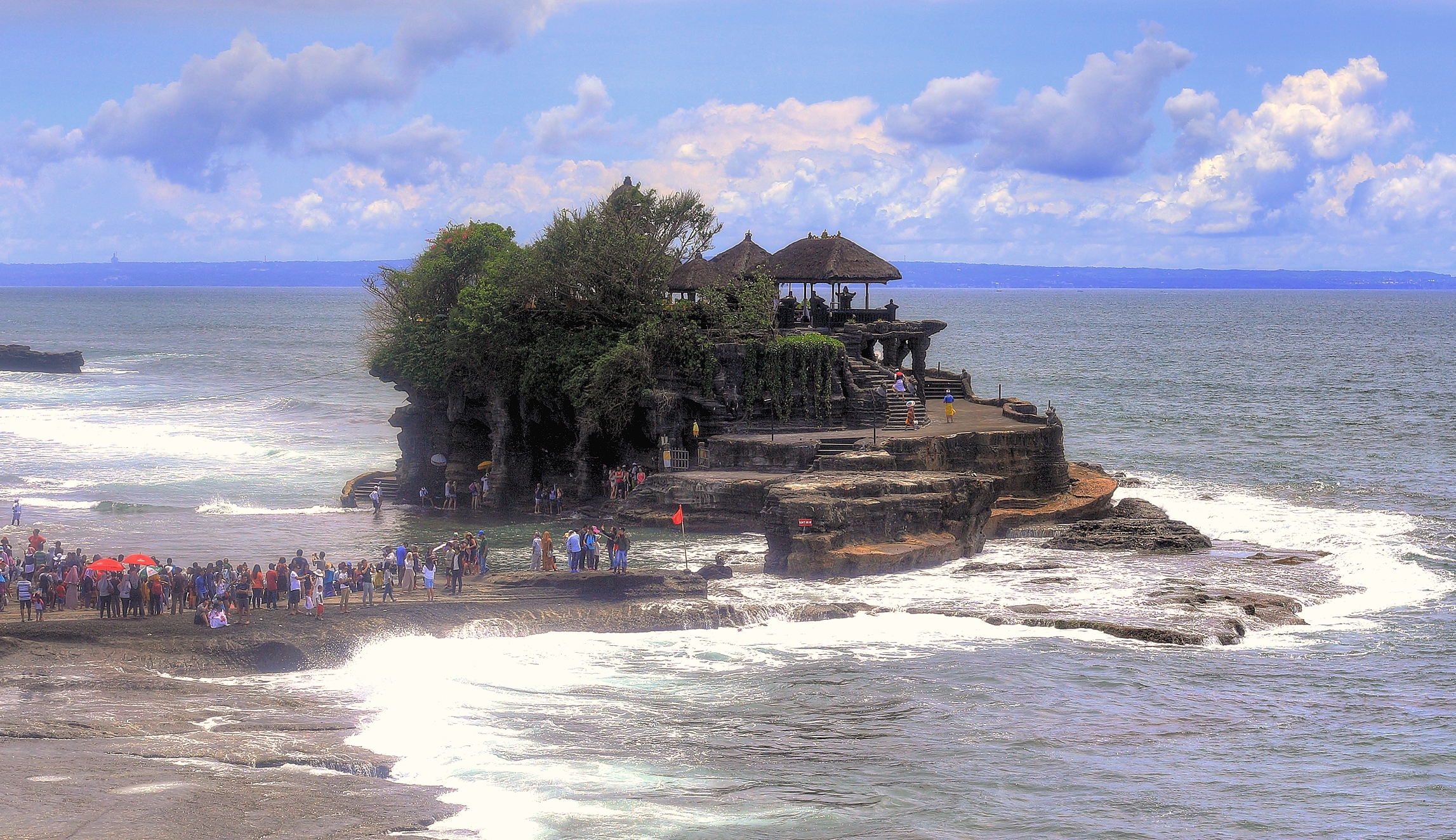 Pura Tanah Lot di pesisir Bali dengan ombak dan langit berawan